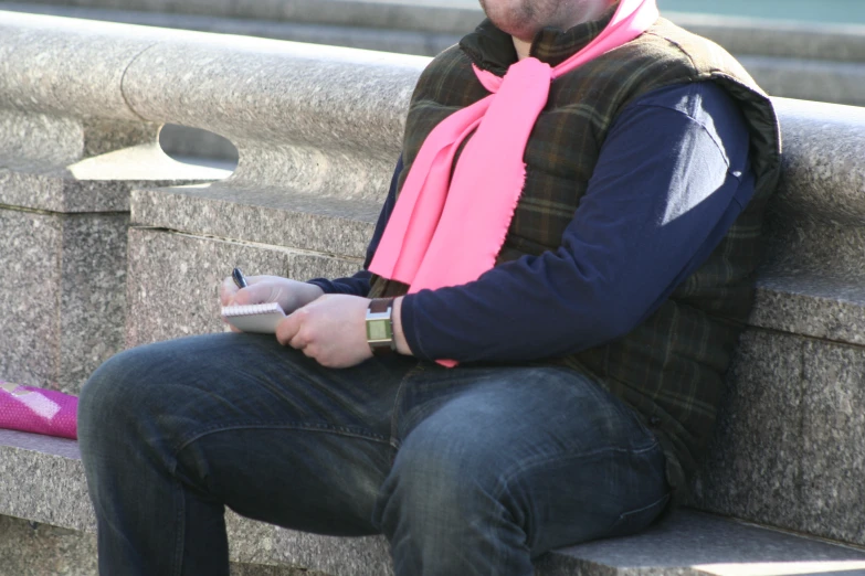 a man sitting on a bench wearing a scarf while writing