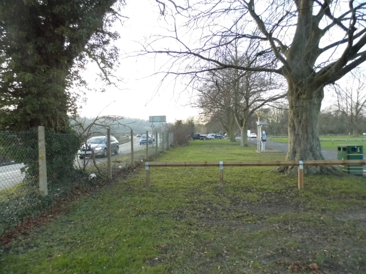 a long fence along the roadside where several cars are parked