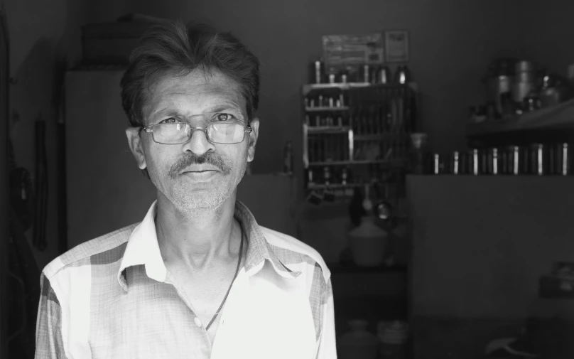 a man wearing glasses standing in front of a counter top