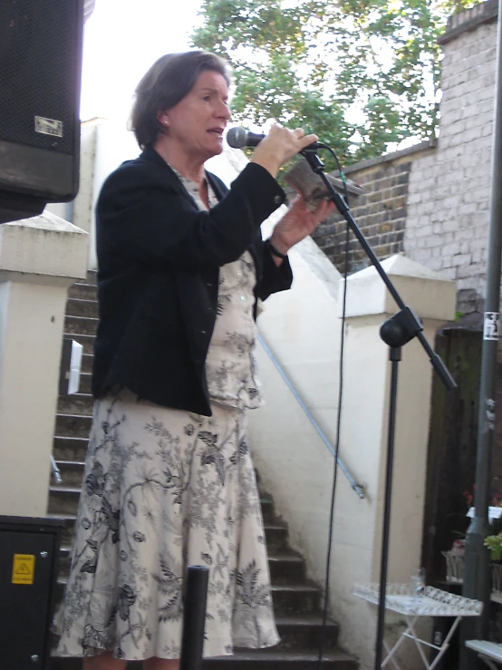 a woman reads from her book while standing near a microphone on the side of a set of steps