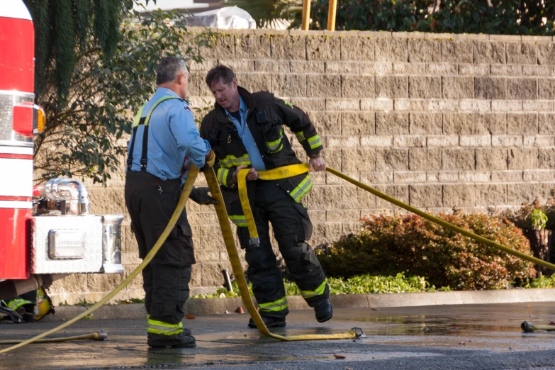 two fire fighters working with a hose to water the sidewalk