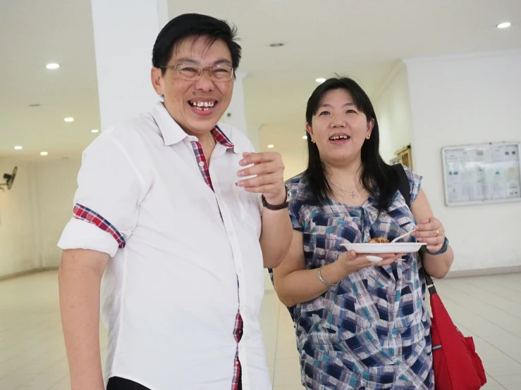 a woman standing next to an asian man and eating a slice of food