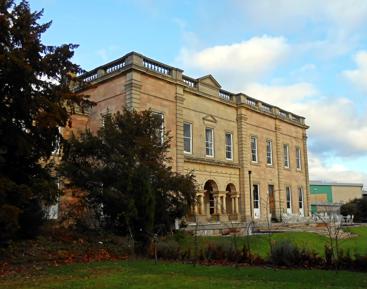 a mansion near some trees and bushes in front of some buildings