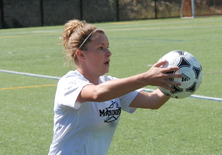 a woman reaching towards the sideline with a soccer ball