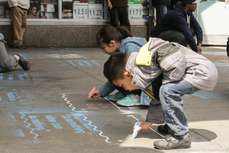 two s writing with sidewalk chalk as others look on