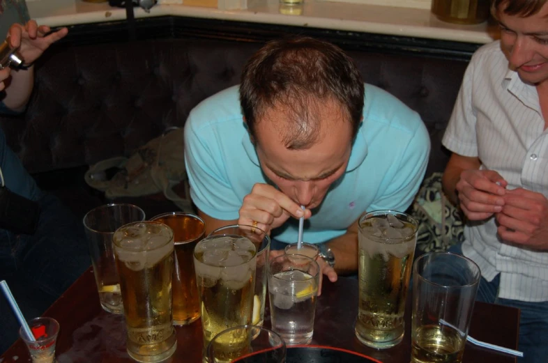 a man drinking from a straw above several glasses