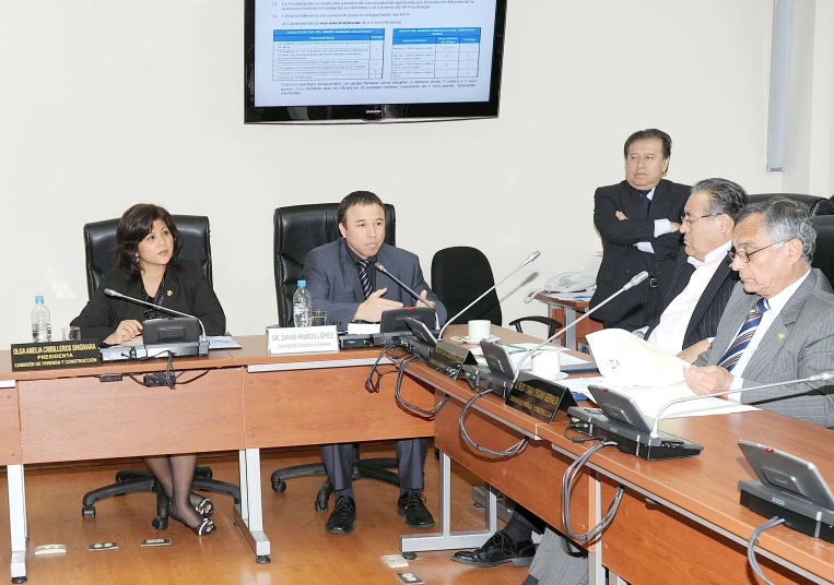 a group of people sitting around a table with a tv mounted on the wall above them