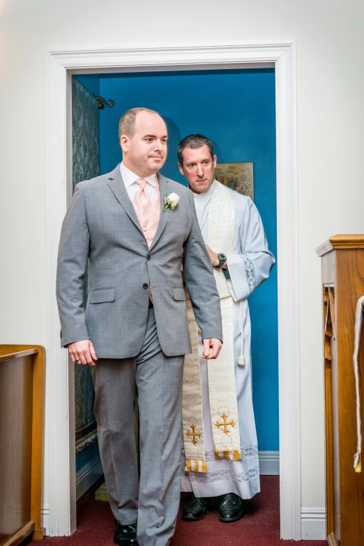 a man in a gray suit and pink tie standing inside of a doorway