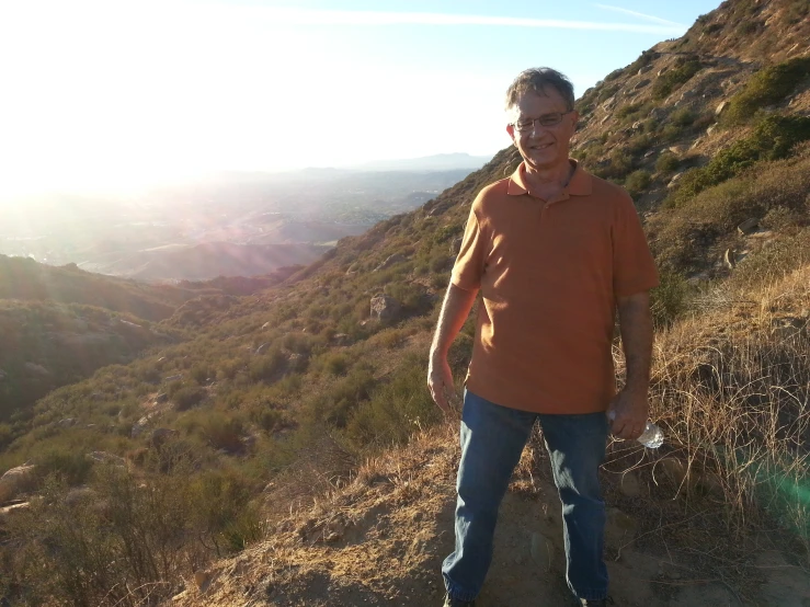 man wearing orange hoodie in the desert looking down at mountains