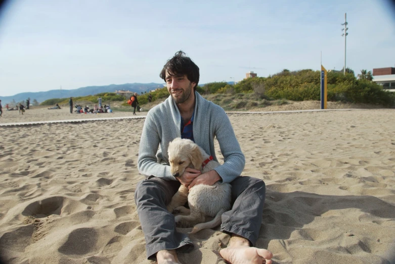 man sitting on a beach with two lambs in his lap