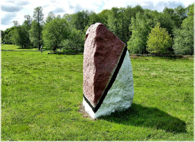 a red rock sitting in the middle of a grass covered field