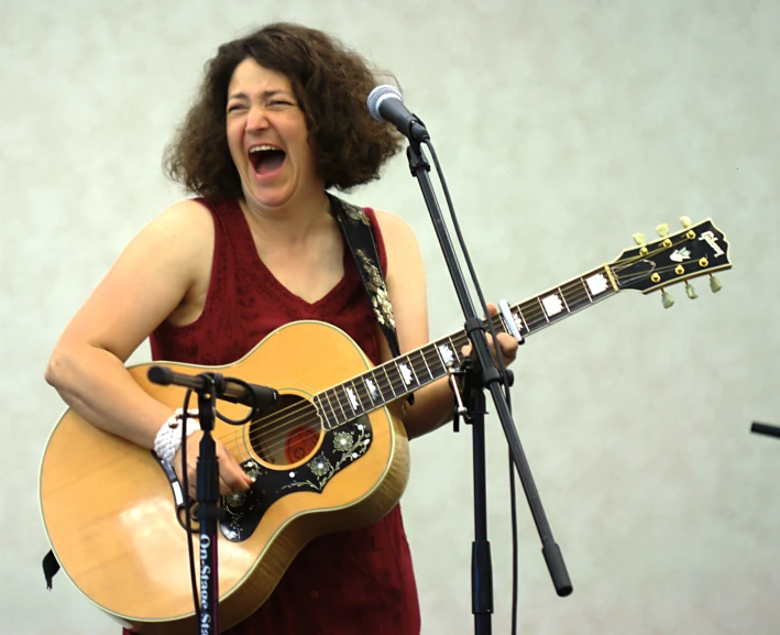 a woman singing and playing the guitar in front of a microphone