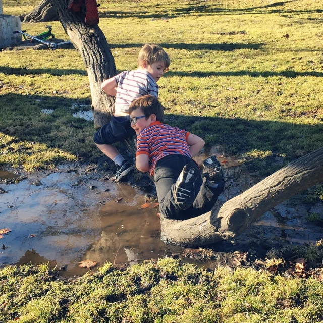 two boys are hanging out in the mud by a tree