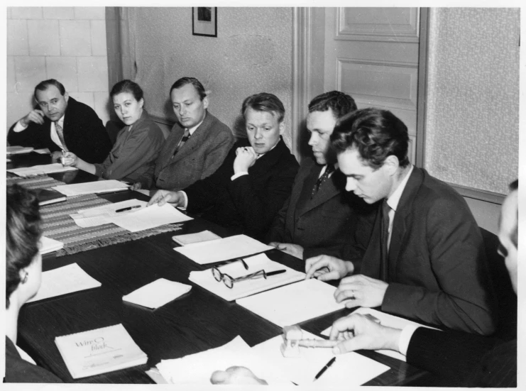 five men sitting at a table writing and making notes