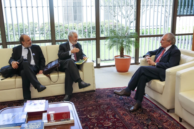 three men in suits and ties sitting on couches