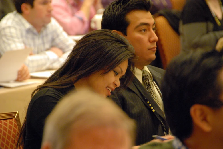 a man and a woman sit close together in a room full of people