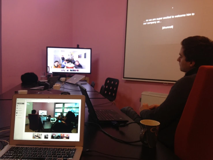 a man is sitting down in a chair watching two people at a computer