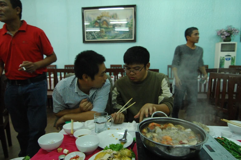 a man standing over some food in front of two other men