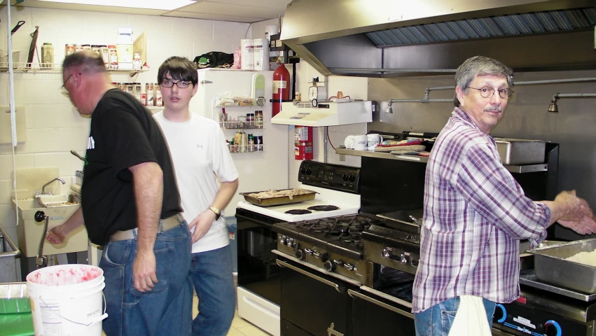 three men are standing in the kitchen talking