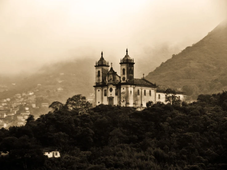 a church surrounded by trees and mountains with fog