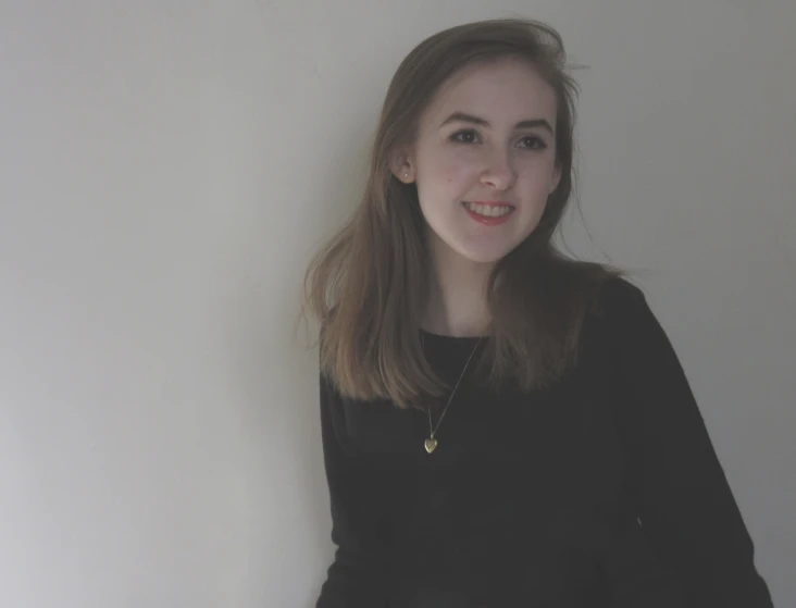 young woman standing in front of white wall with one eye closed