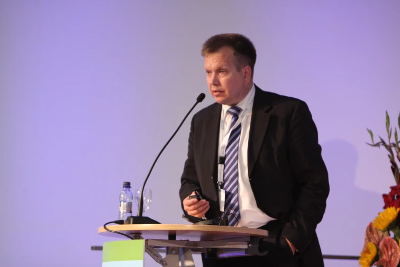 the man in a suit stands near a podium and speaks into a microphone