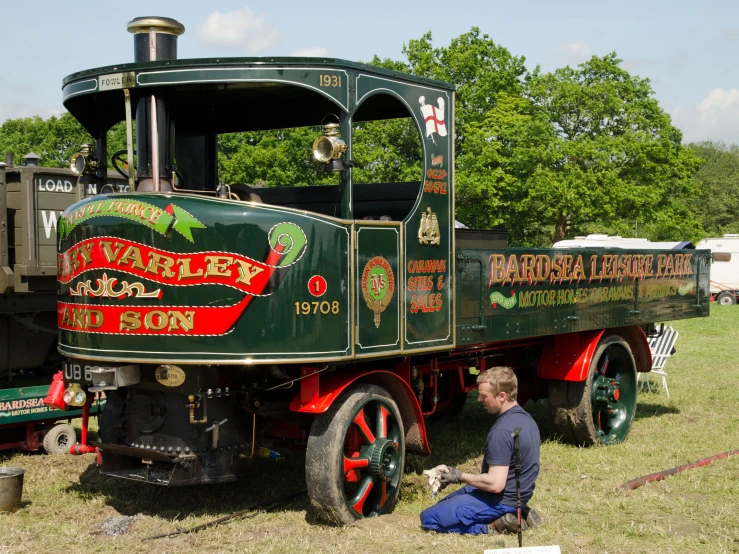 man sitting on the ground next to an antique green and red train