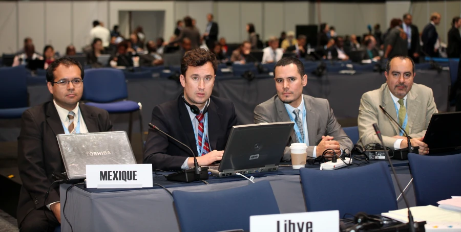 four men seated at tables with laptops while listening to a presentation