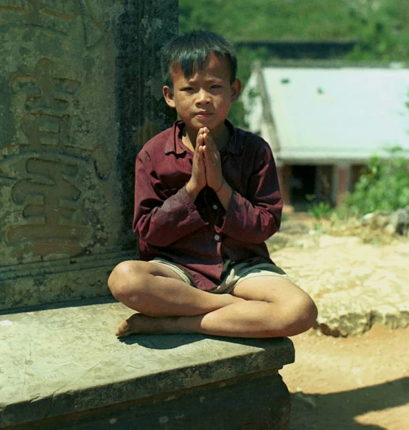a boy sitting in front of an obelisk with his hands folded