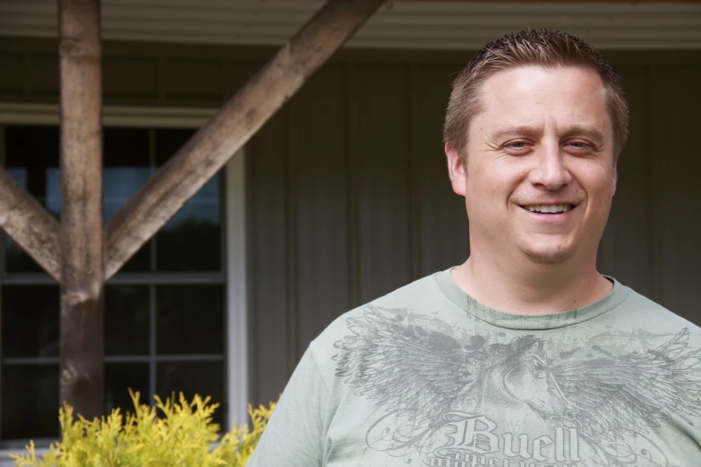 a man wearing a green t - shirt standing outside of a house