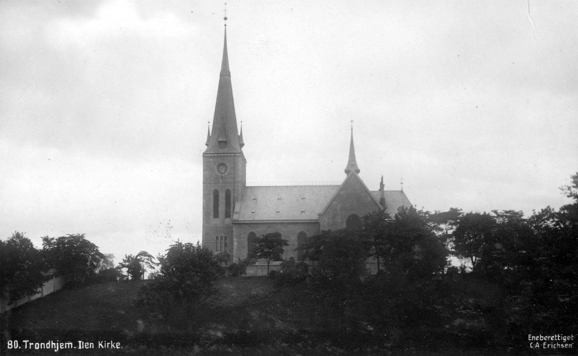 a tall white church with a steeple standing in a forested area