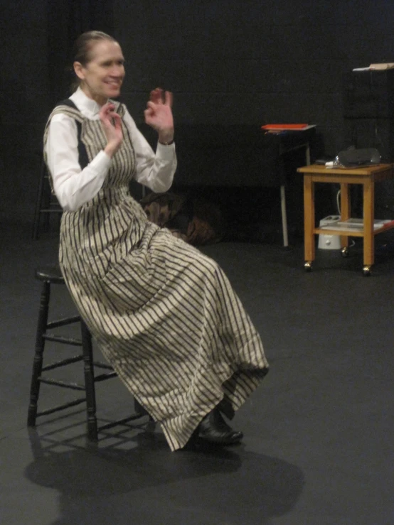 a woman sitting on top of a wooden chair with her hands clasped