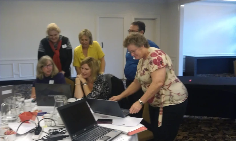 a group of people are gathered around a table with laptops