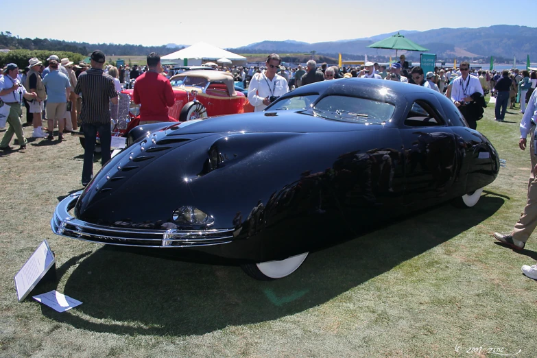 people standing around and watching a classic black car