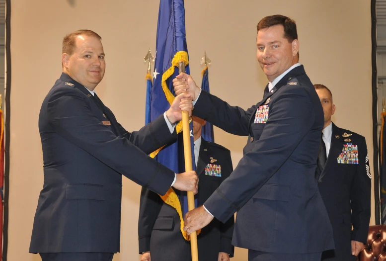 two men in military uniforms are holding the flag pole