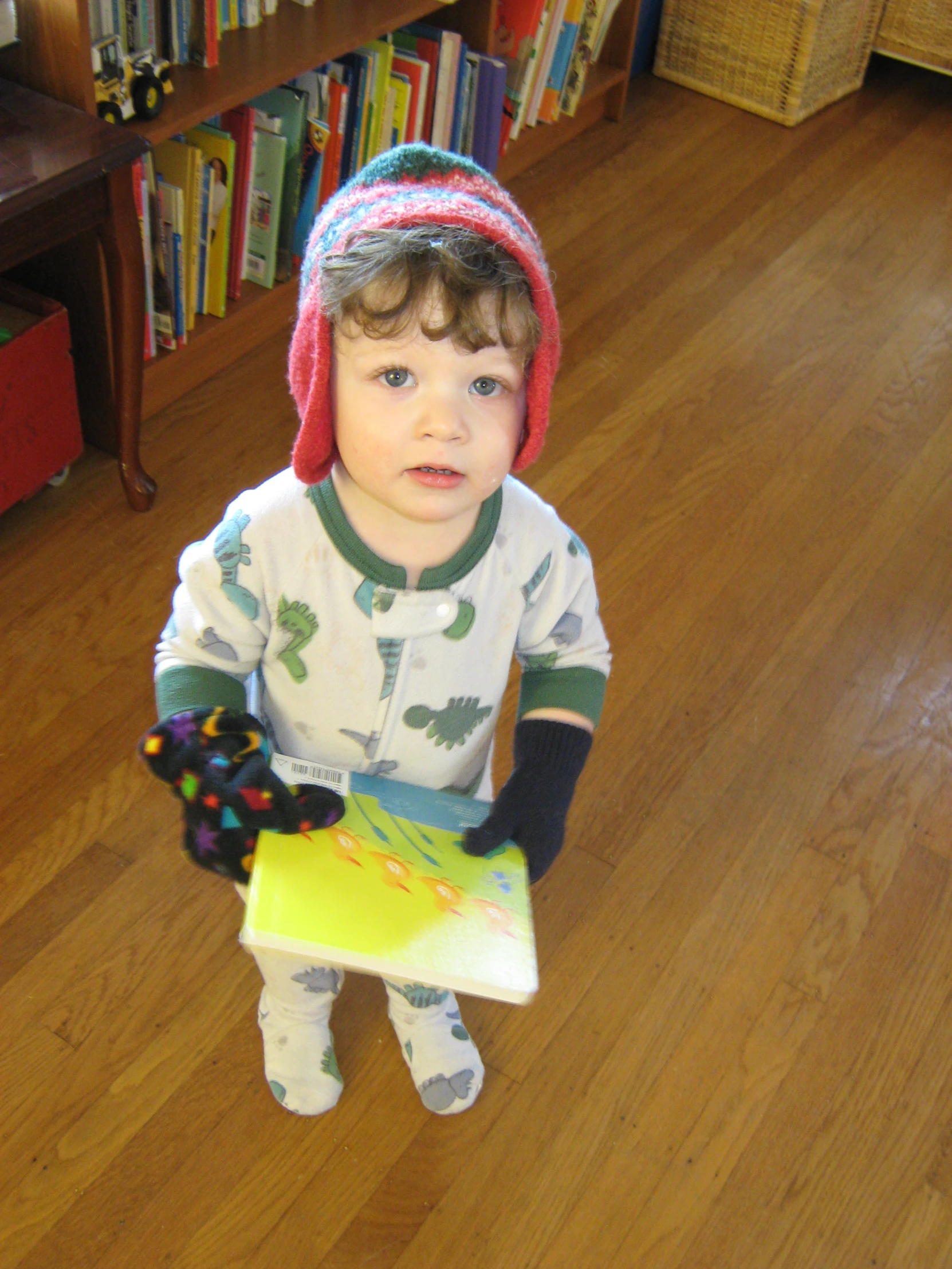 small child in pajamas and a red beanie holding a yellow item