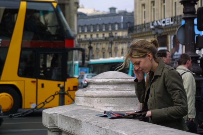 a woman looks down at her cell phone in front of a bus