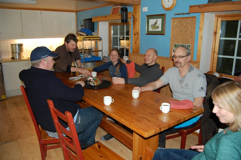 five people eating and drinking around a wooden table