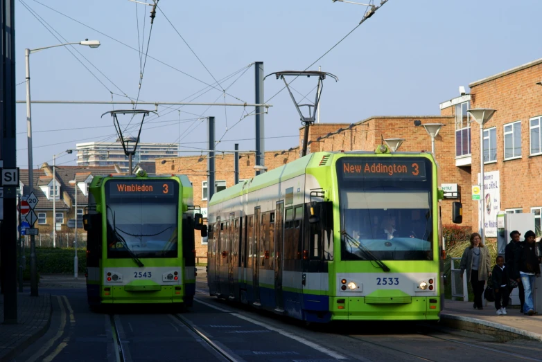 two green and blue commuter buses sitting in a stop at a train station