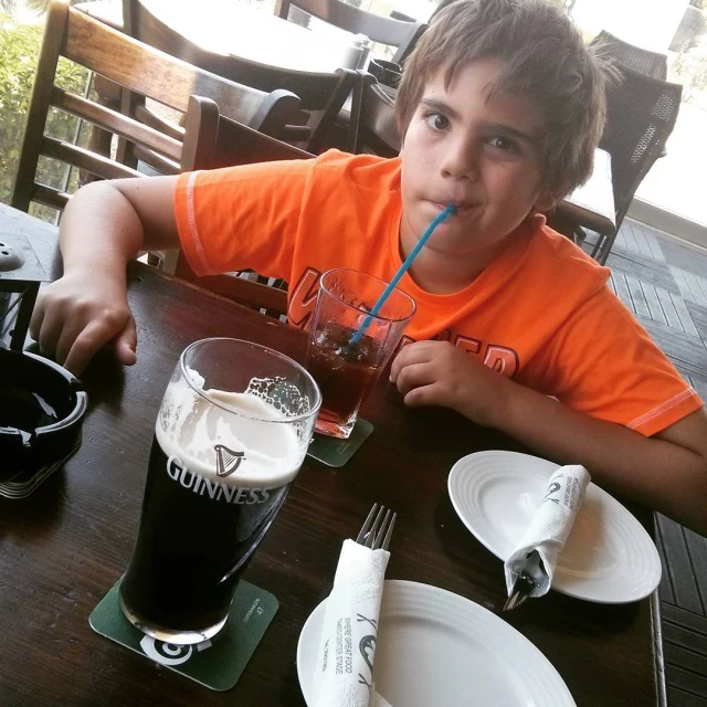a boy is sitting at a table with a beverage in his mouth