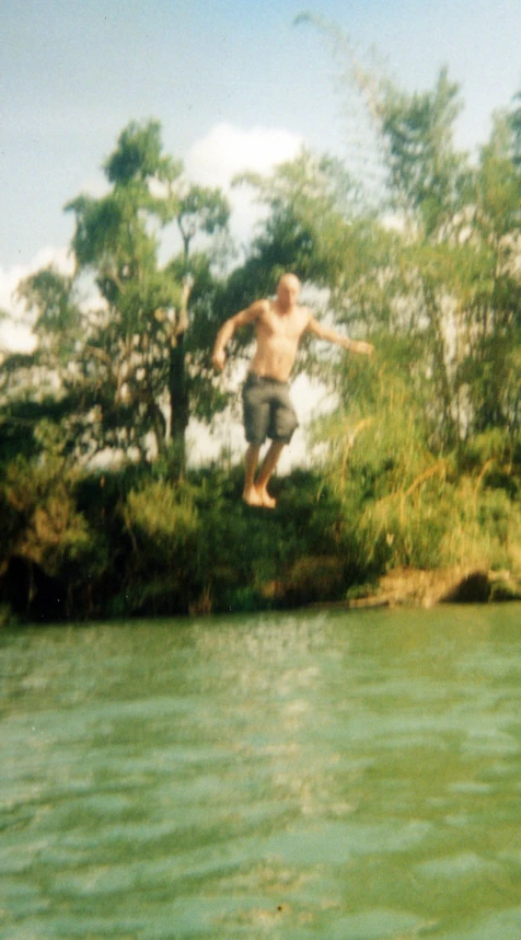man doing skateboard jump off a small ledge above water