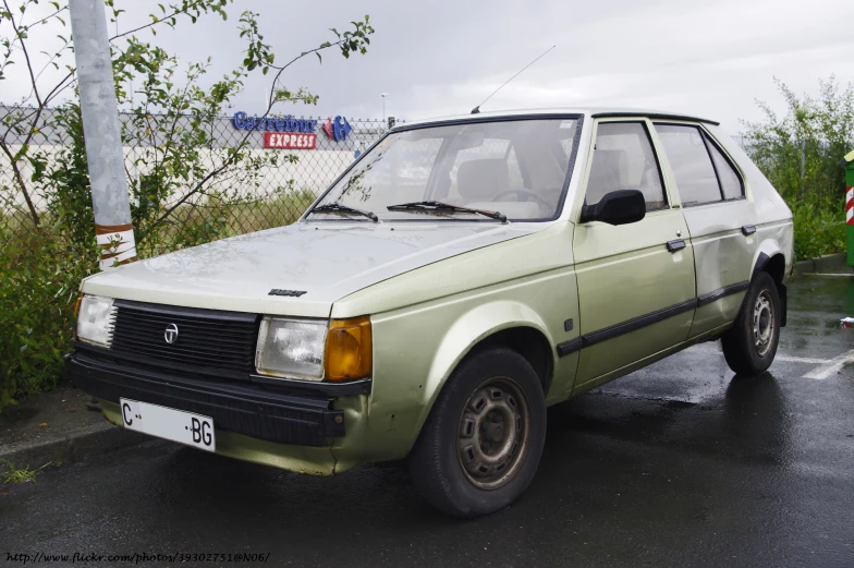 an old green toyota hatchback sits parked on the side of the road