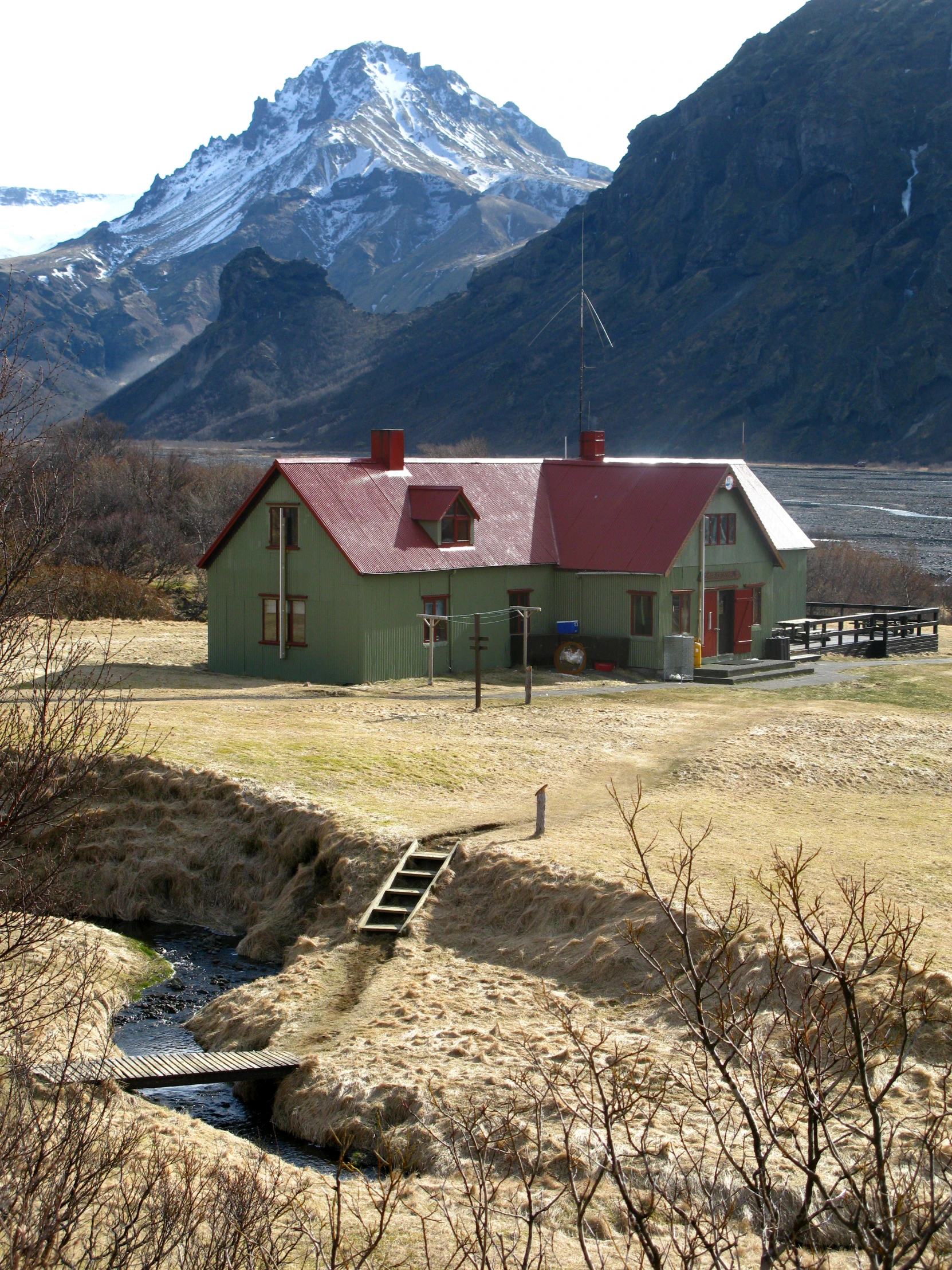 a small red roofed cabin is in the middle of some mountains