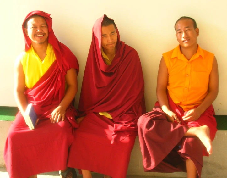 three men wearing bright colored robes are sitting on a wall