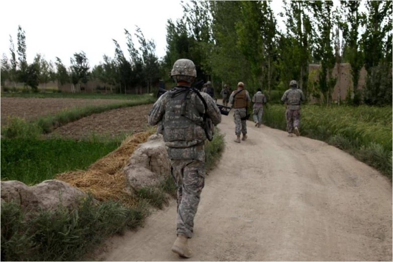 some men in camoflads are walking on a dirt road