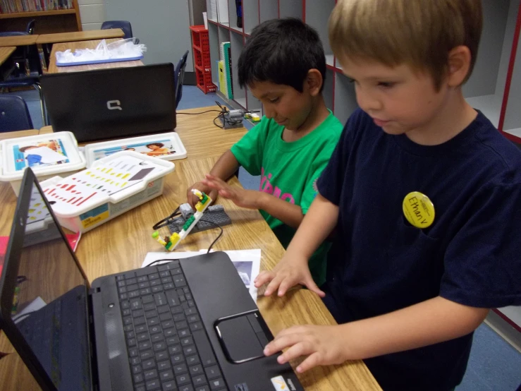 two children sitting at a table playing with a laptop