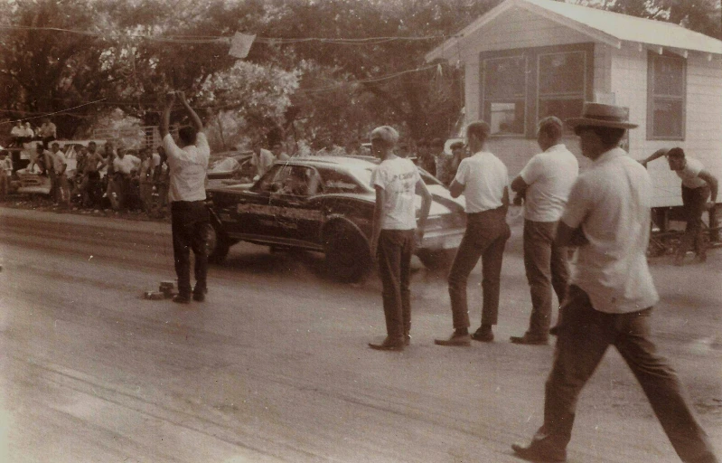 an old pograph of several men and a car with two men standing by it