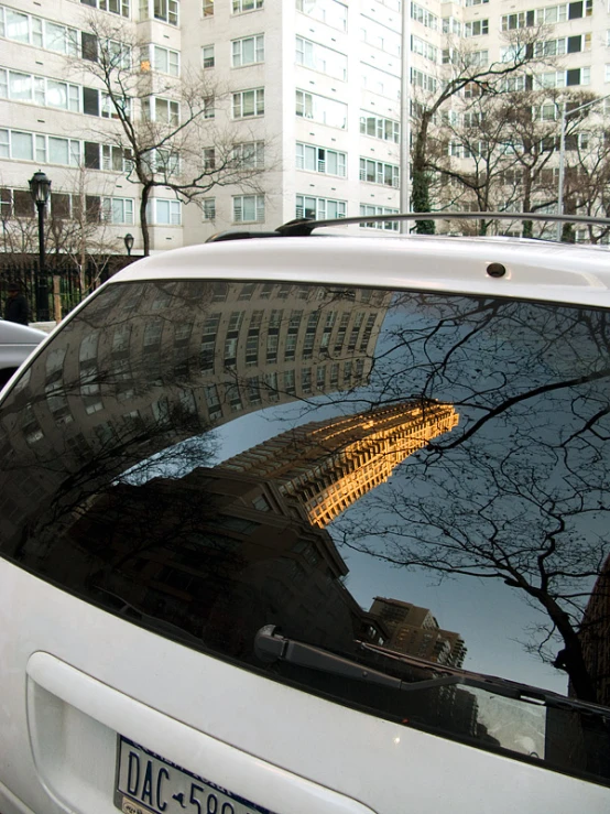 a car parked in a parking lot with trees and buildings reflected on it