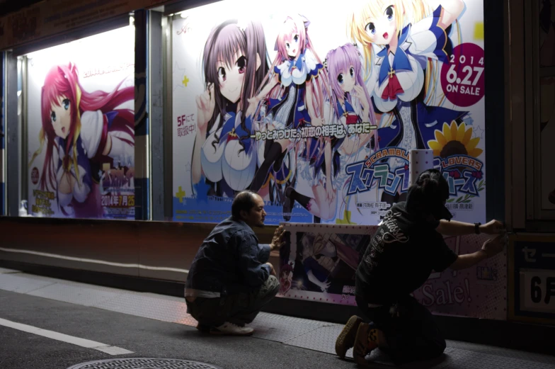 the two men are sitting down painting a giant anime advertit