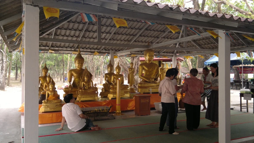 there are people sitting in front of the golden buddha statues